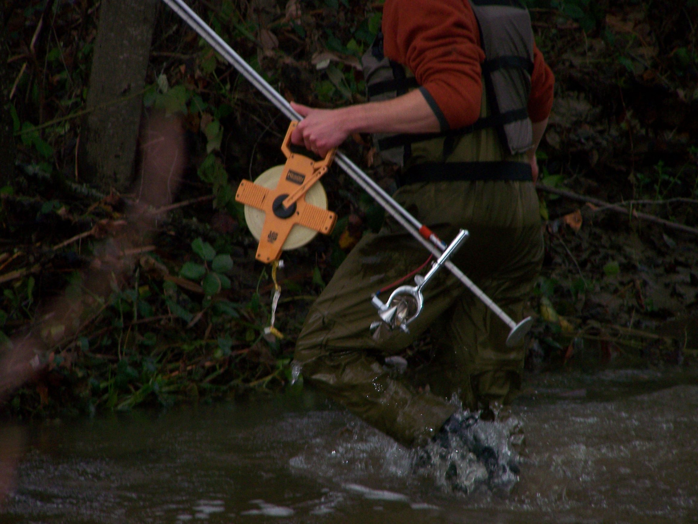 person walking in creek holding field equipment